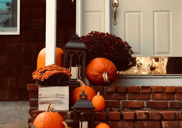 A nicely decorated brick stoop adorned with fall mums, pumpkins and candles inside lanterns.