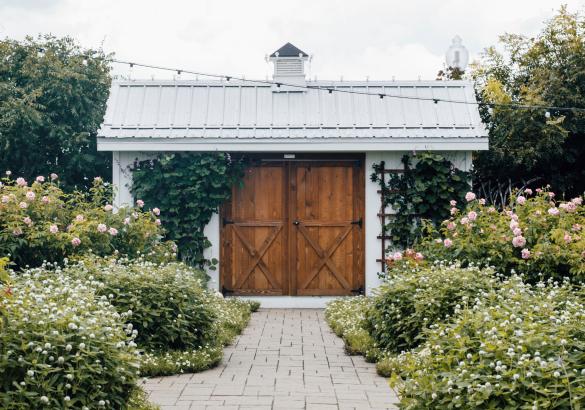 A well kept stone garden walkway leads to an outdoor shed with rustic barn doors.