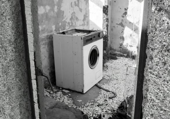 Black and white photo of an old washing machine sitting in an old dank basement 