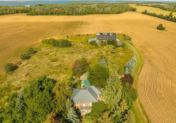 Drone shot of well treed lot with old barn and farmhouse in foreground with property surrounded by farmland.