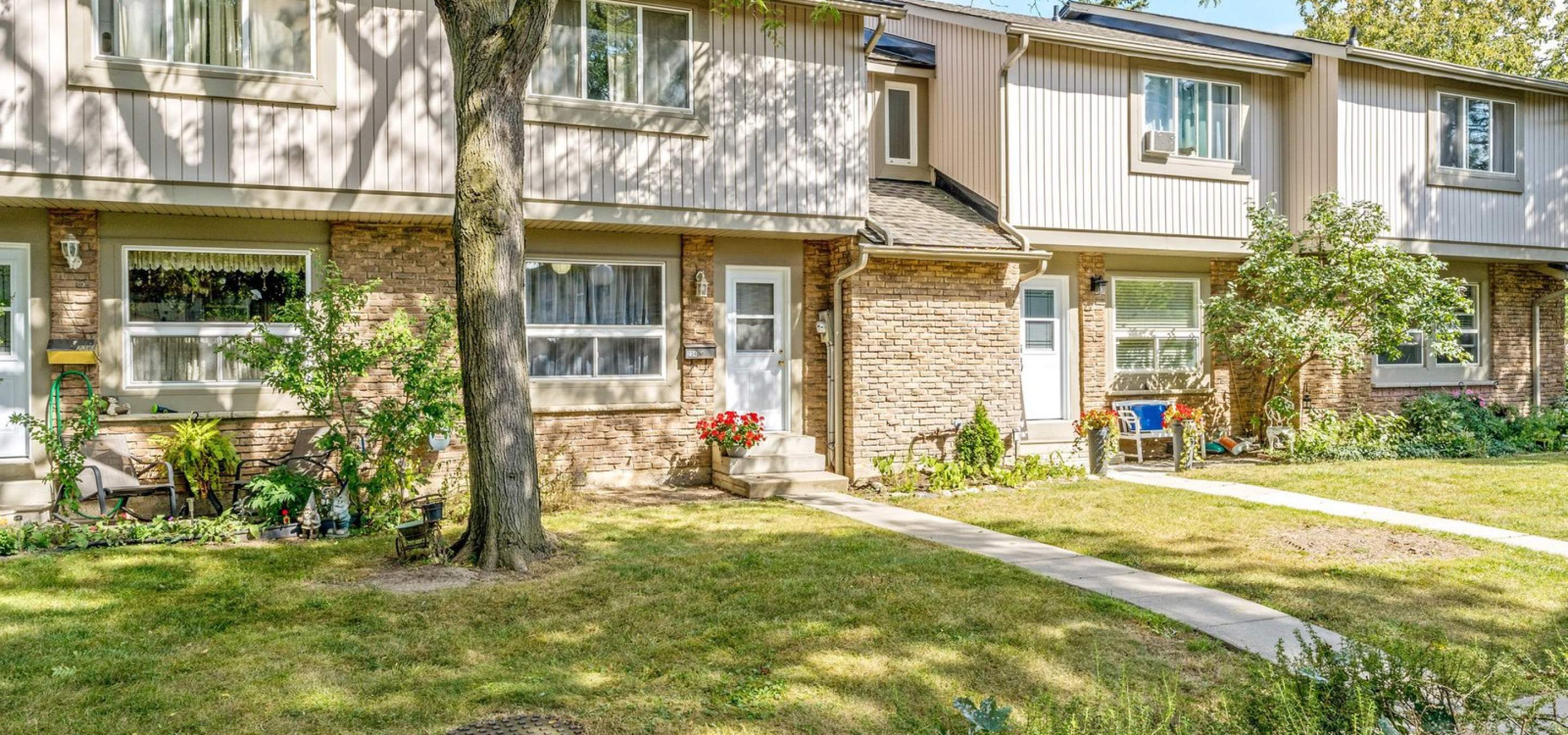 Exterior summer photo of condo unit with green grass, dedicated walkway and flowers decorating the doorway area